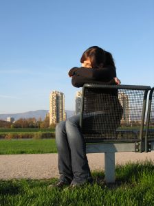 Žena sedící na lavičce v parku se smutnou náladou